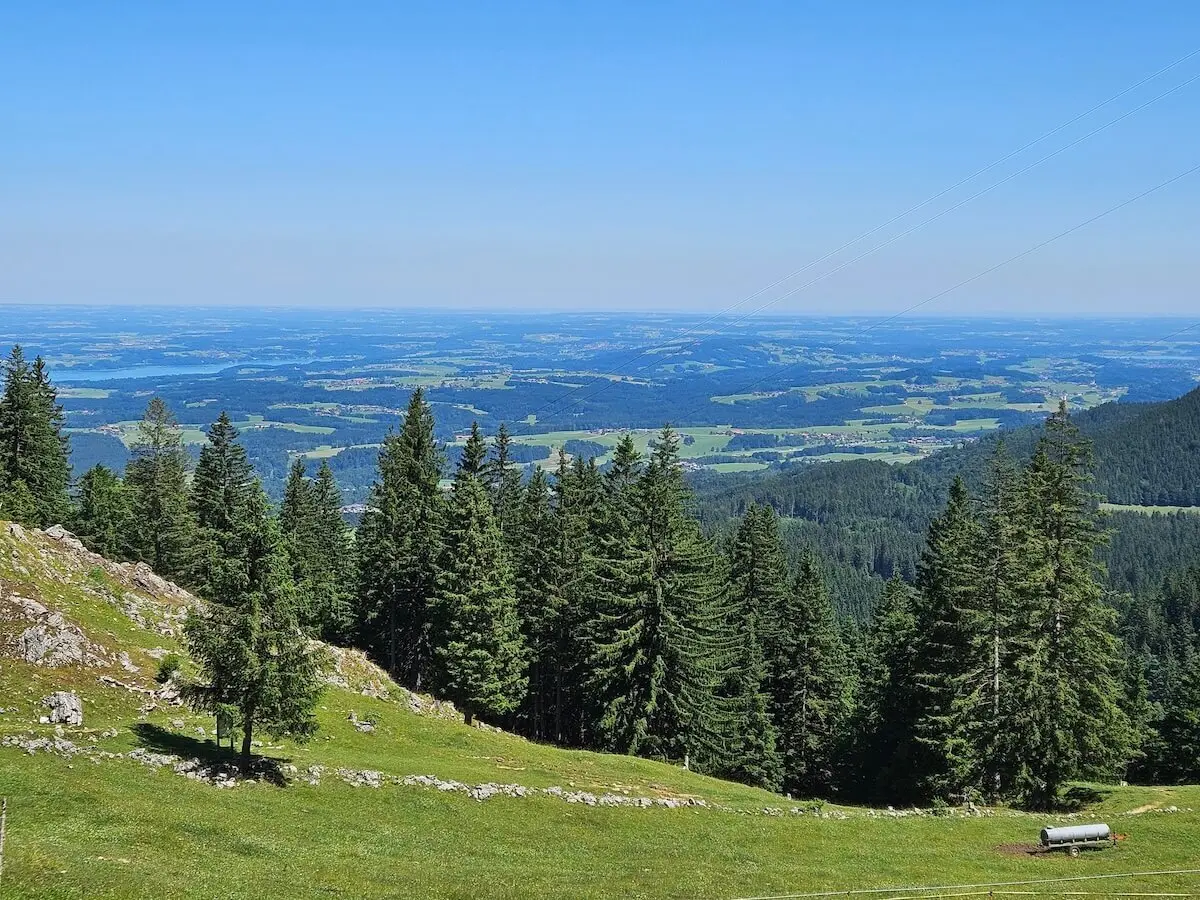 Vom Hochries-Panoramaweg aus öffnet sich der Blick auf grüne Wälder, Felder und ferne Siedlungen bei klarem Himmel. | © DAV Markt Schwaben | Foto Hubert Inhofer