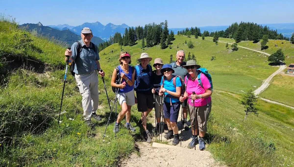 Sieben ältere Wanderer stehen mit Ausrüstung auf einem Pfad in alpiner Landschaft mit weitem Blick über Hügel und Täler. | © DAV Markt Schwaben | Foto Hubert Inhofer