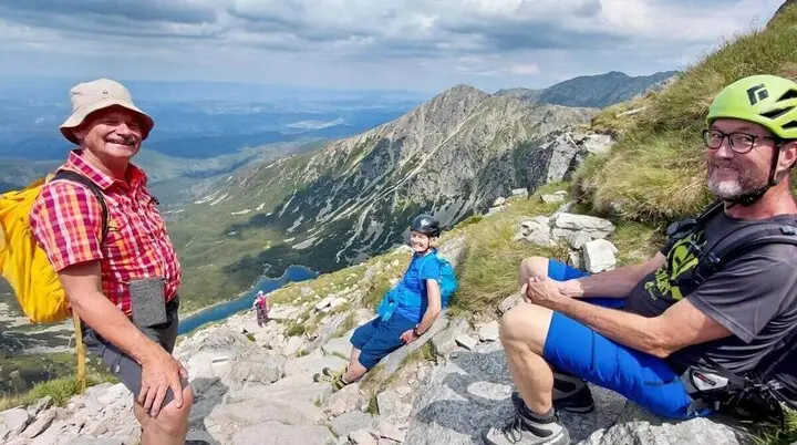 Drei Wandernde sitzen auf Felsen oberhalb eines Bergsees; im Hintergrund steile Hänge, Wolken und weite Aussicht ins Tal. | © DAV Markt Schwaben | Foto Sabine Hainz