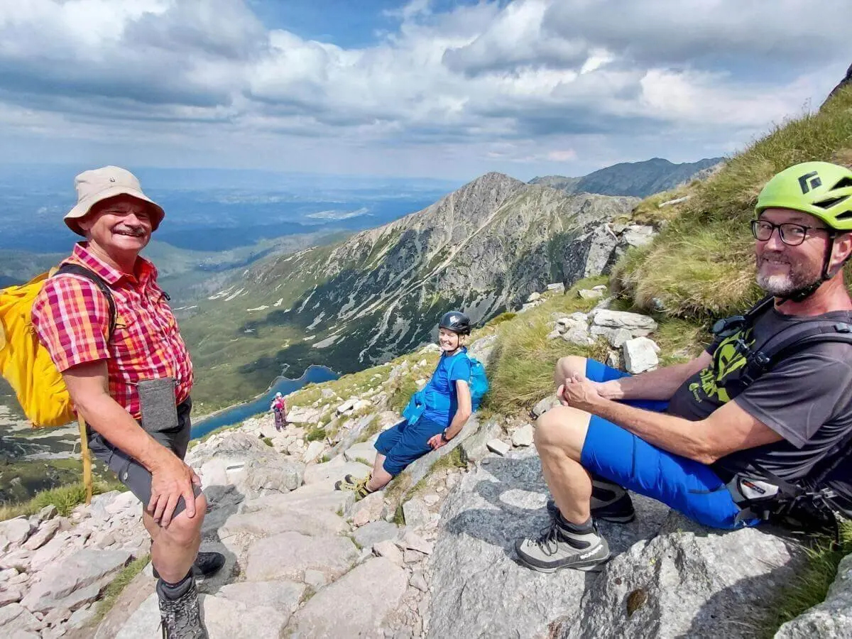 Drei Wandernde sitzen auf Felsen oberhalb eines Bergsees; im Hintergrund steile Hänge, Wolken und weite Aussicht ins Tal. | © DAV Markt Schwaben | Foto Sabine Hainz