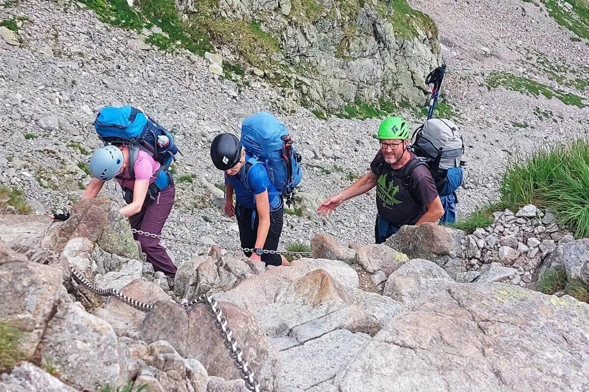 Vier Wandernde steigen mit Helm und Rucksack über steilen Felsgrat; sie sichern sich mit Ketten im nebligen Hochgebirge. | © DAV Markt Schwaben | Foto Lutz Gründel