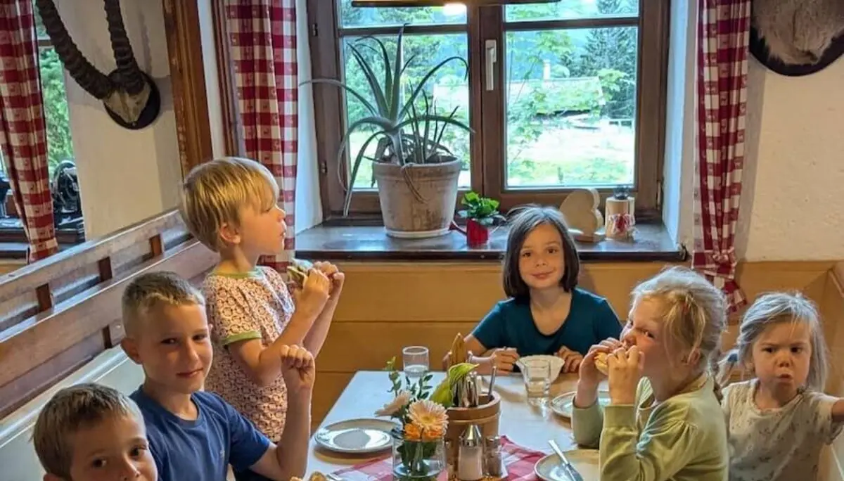 Kinder sitzen gemeinsam am Holztisch in der Schönfeldhütte und essen bei gemütlicher Abendstimmung. | © DAV Markt Schwaben | Foto Familiengruppe