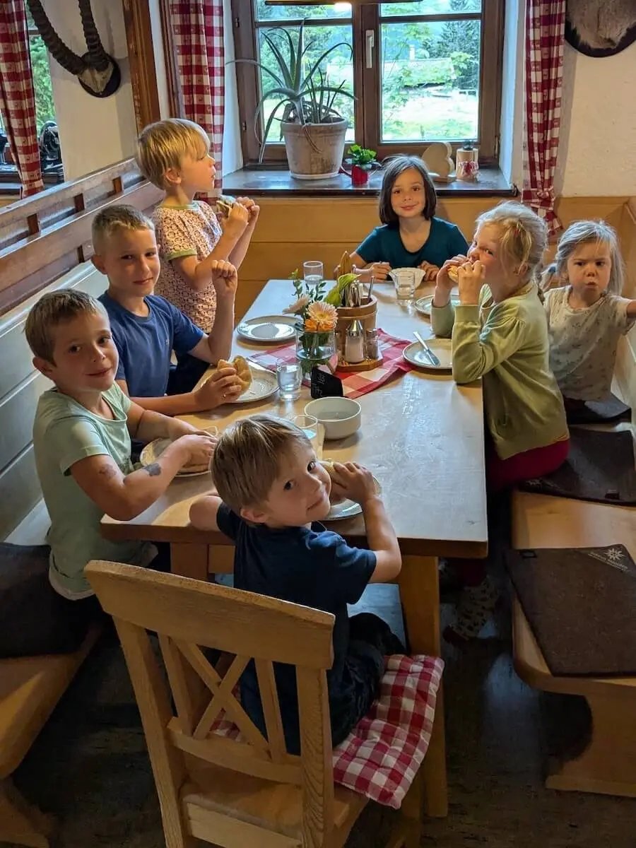 Kinder sitzen gemeinsam am Holztisch in der Schönfeldhütte und essen bei gemütlicher Abendstimmung. | © DAV Markt Schwaben | Foto Familiengruppe