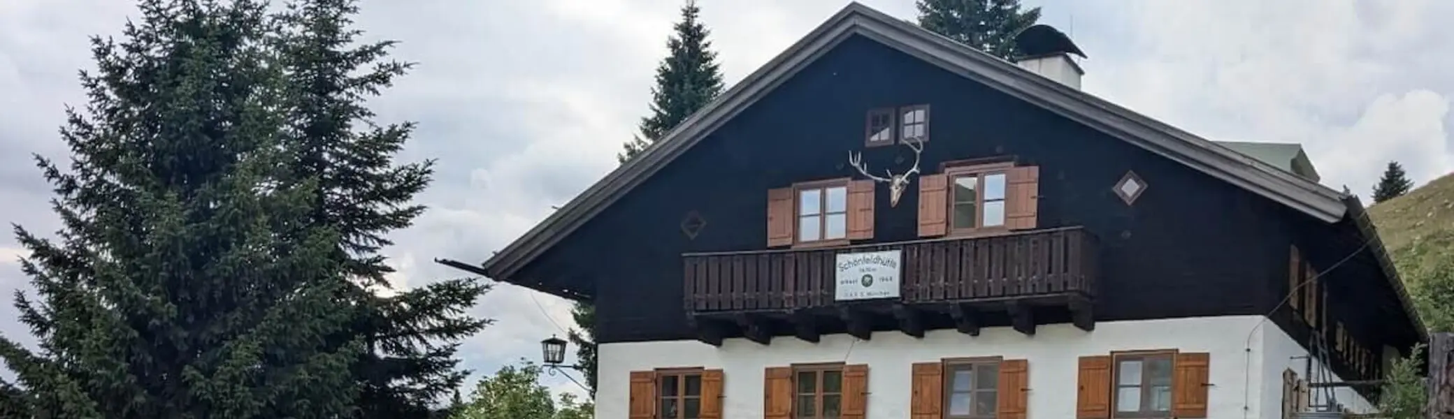 Fröhliche Familiengruppe posiert vor der Schönfeldhütte. Kinder und Erwachsene stehen lachend beisammen, einige winken. | © DAV Markt Schwaben | Foto Familiengruppe