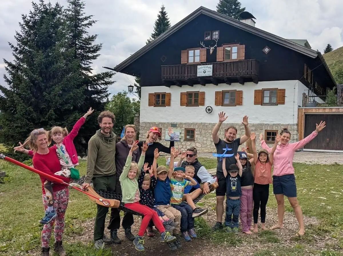 Fröhliche Familiengruppe posiert vor der Schönfeldhütte. Kinder und Erwachsene stehen lachend beisammen, einige winken. | © DAV Markt Schwaben | Foto Familiengruppe