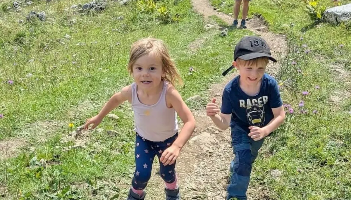 Zwei Kinder wandern über einen steinigen Pfad im Grünen. Im Hintergrund begleiten Erwachsene die Bergtour durch hügelige Landschaft. | © DAV Markt Schwaben | Foto Familiengruppe
