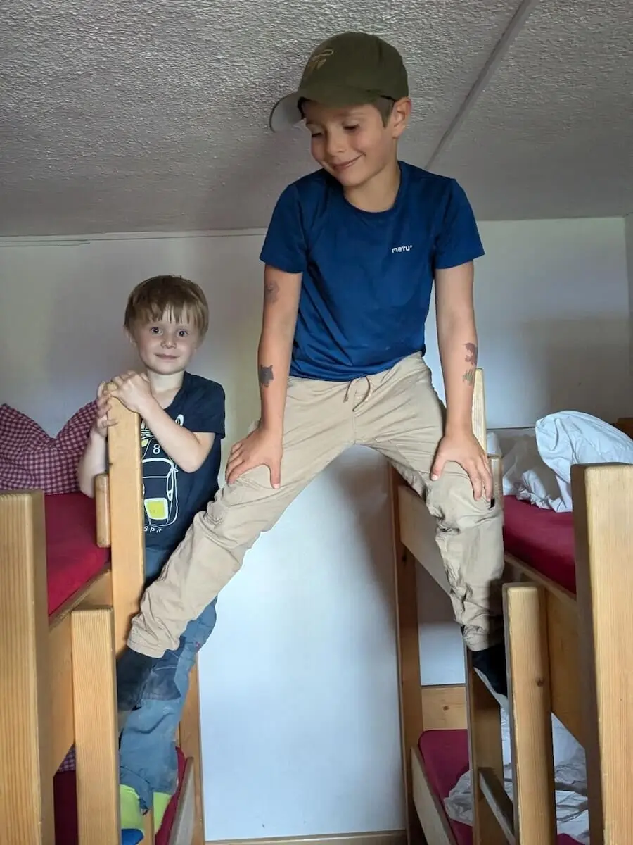 Zwei Kinder spielen lebhaft auf Etagenbetten in einer Berghütte. Einer balanciert über die obere Bettkante, der andere steht unten. | © DAV Markt Schwaben | Foto Familiengruppe