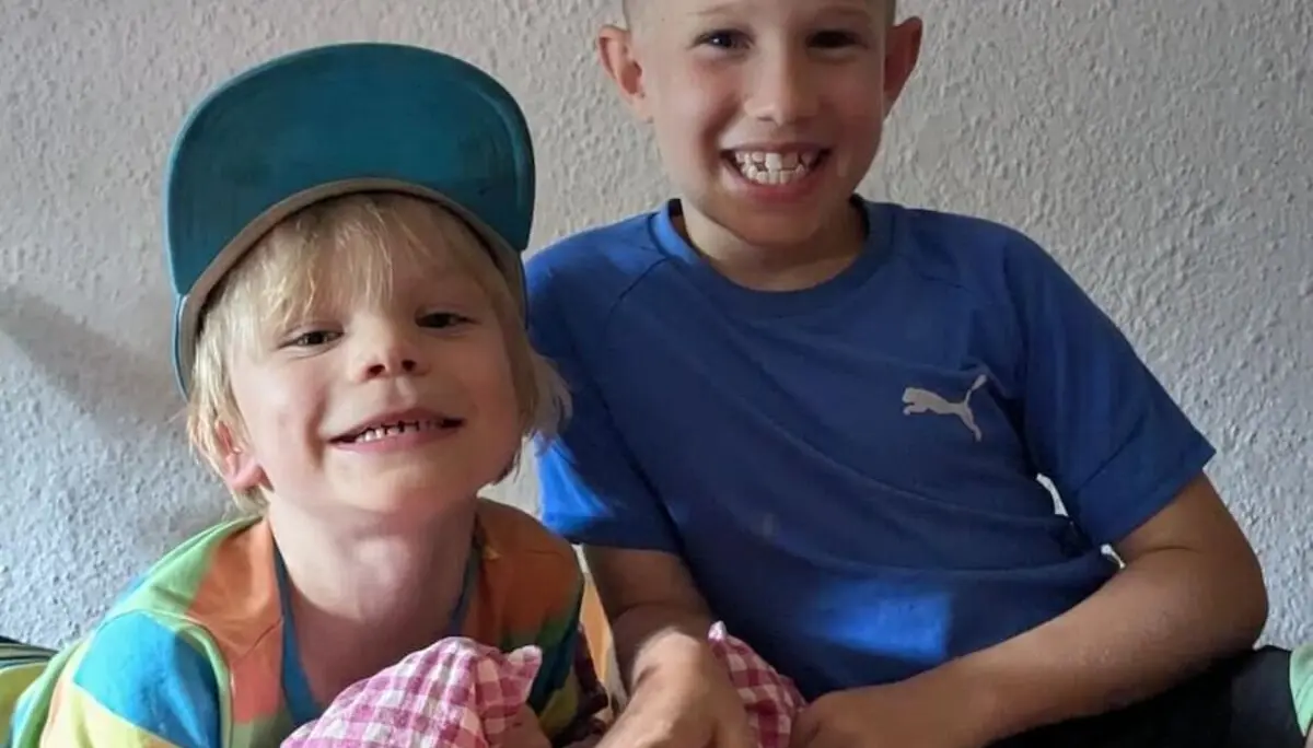 Zwei Kinder sitzen entspannt auf einem Holzbett mit roter Decke. Einer hält ein Kissen, beide genießen die Hüttenatmosphäre. | © DAV Markt Schwaben | Foto Familiengruppe