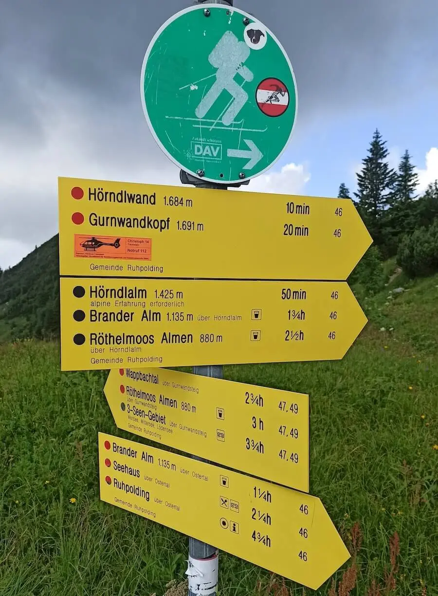 Gelbe Wanderschilder bei Ruhpolding zeigen Wanderwege und Zeiten zur Hördlwand, Almen und Seenregion. | © DAV Markt Schwaben