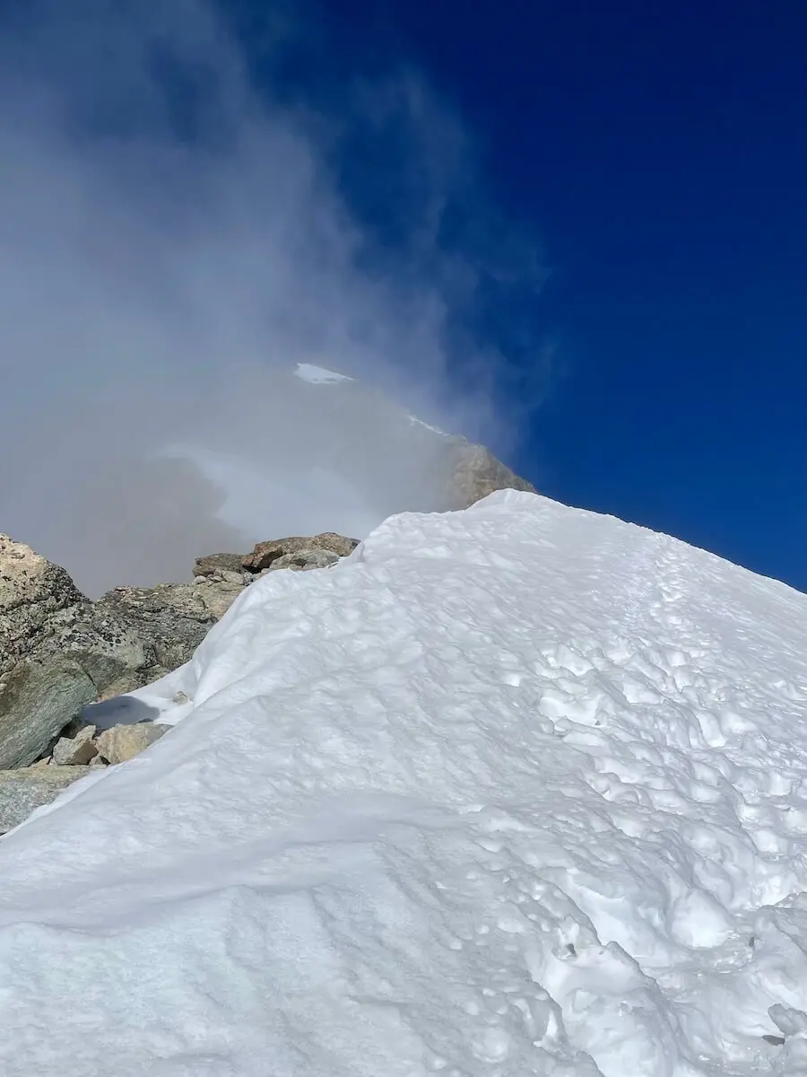 Auf einer schneebedeckten Westalpenflanke führen Fußspuren bergauf – Nebelschwaden verhüllen den Gipfel am Horizont. | © DAV Markt Schwaben | Christian Reischl