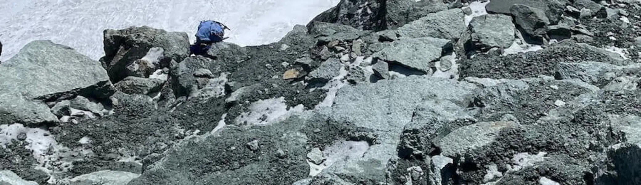 Ein Bergsteiger in blauer Jacke durchquert felsiges Gelände mit Schnee im Hochgebirge der Westalpen – Nebel am Gipfel. | © DAV Markt Schwaben | Christian Reischl