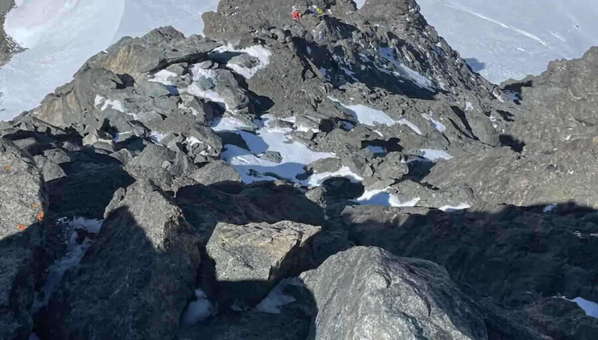 Zwei Bergsteiger im roten und gelben Outfit steigen durch felsiges, teils verschneites Gelände der Westalpen – steil und ausgesetzt. | © DAV Markt Schwaben | Christian Reischl