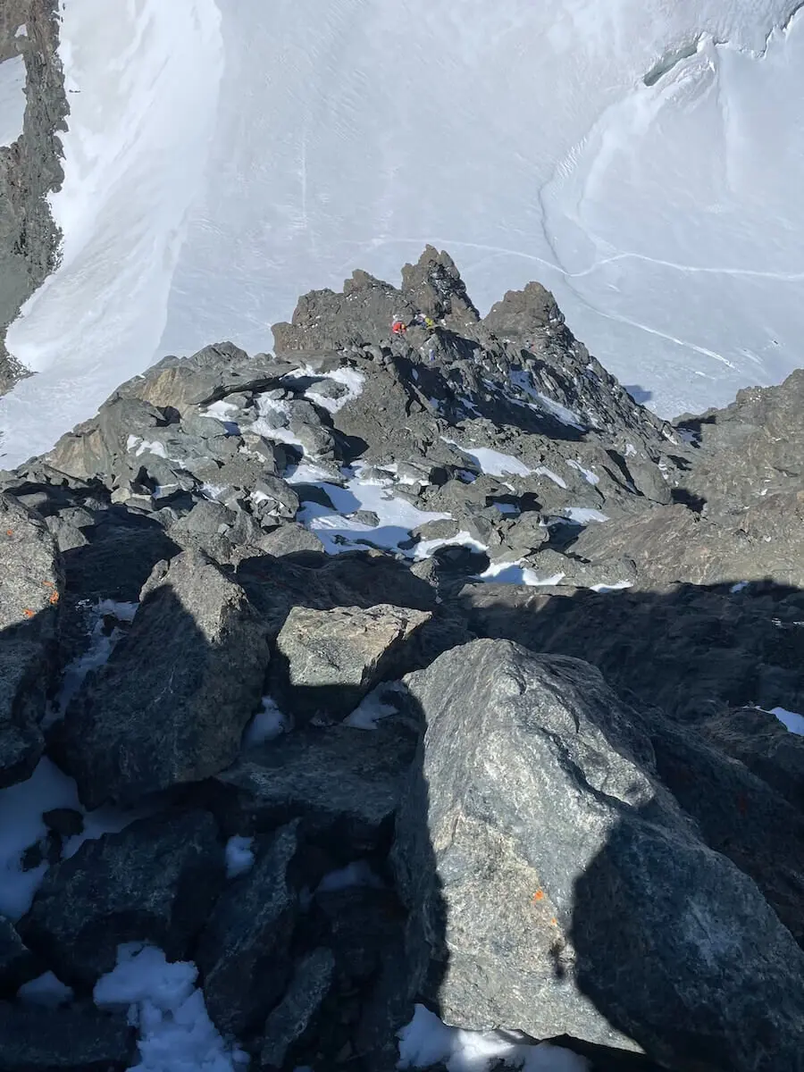 Zwei Bergsteiger im roten und gelben Outfit steigen durch felsiges, teils verschneites Gelände der Westalpen – steil und ausgesetzt. | © DAV Markt Schwaben | Christian Reischl