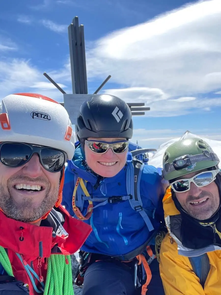 Drei Bergsteiger stehen vor einem Gipfelkreuz in den Westalpen – klare Sicht, Schnee und Kletterausrüstung zeigen den Moment des Erfolgs. | © DAV Markt Schwaben | Christian Reischl