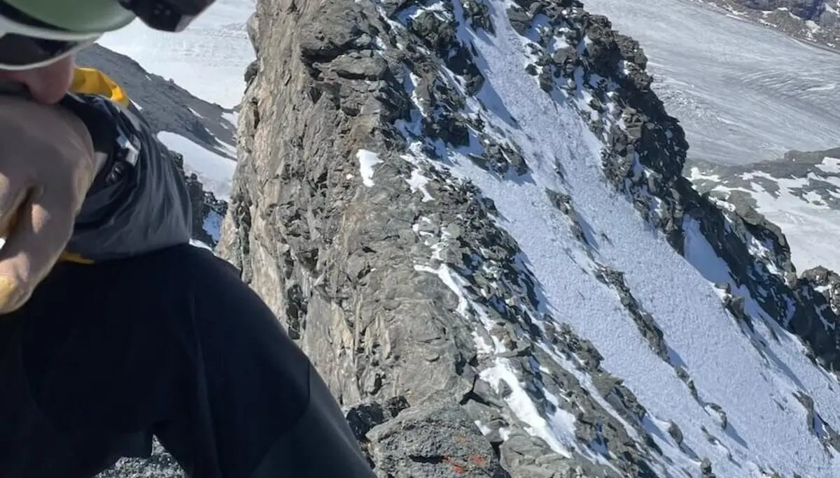 Ein Bergsteiger sitzt mit Helm und Steigeisen auf einem felsigen Grat der Westalpen – im Hintergrund Gletscher und klare Bergsicht. | © DAV Markt Schwaben | Christian Reischl