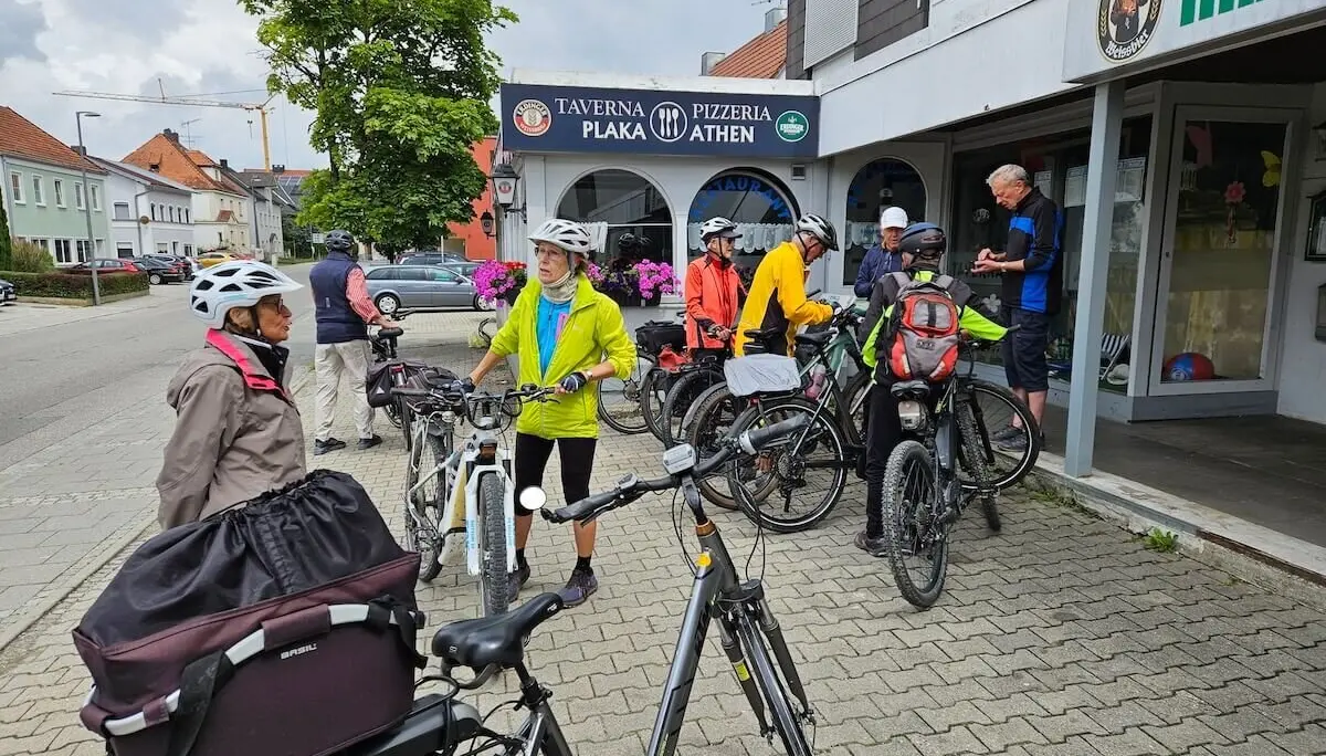 Senior:innen mit Helmen und Fahrrädern stehen plaudernd vor einer Taverne – Gruppenpause bei der Radtour. | © DAV Markt Schwaben | Seniorengruppe