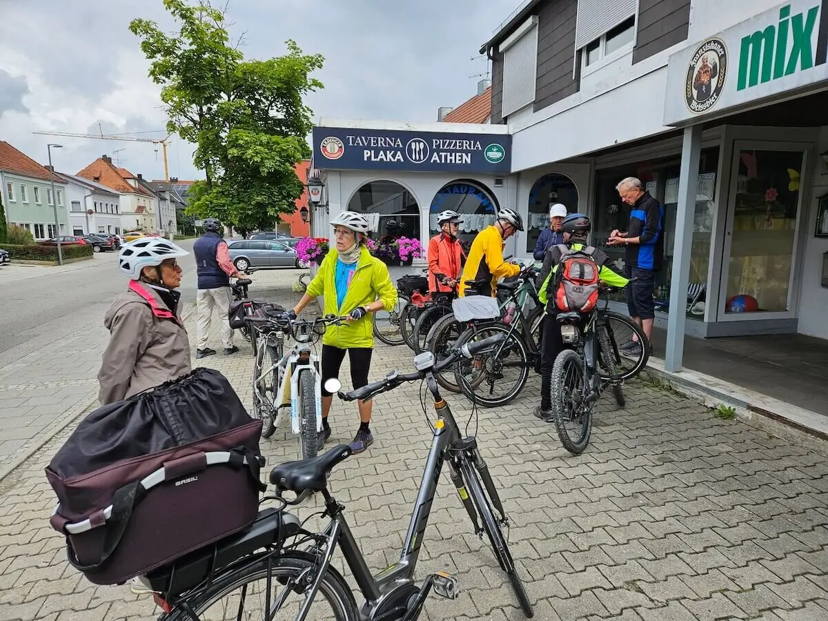 Senior:innen mit Helmen und Fahrrädern stehen plaudernd vor einer Taverne – Gruppenpause bei der Radtour. | © DAV Markt Schwaben | Seniorengruppe