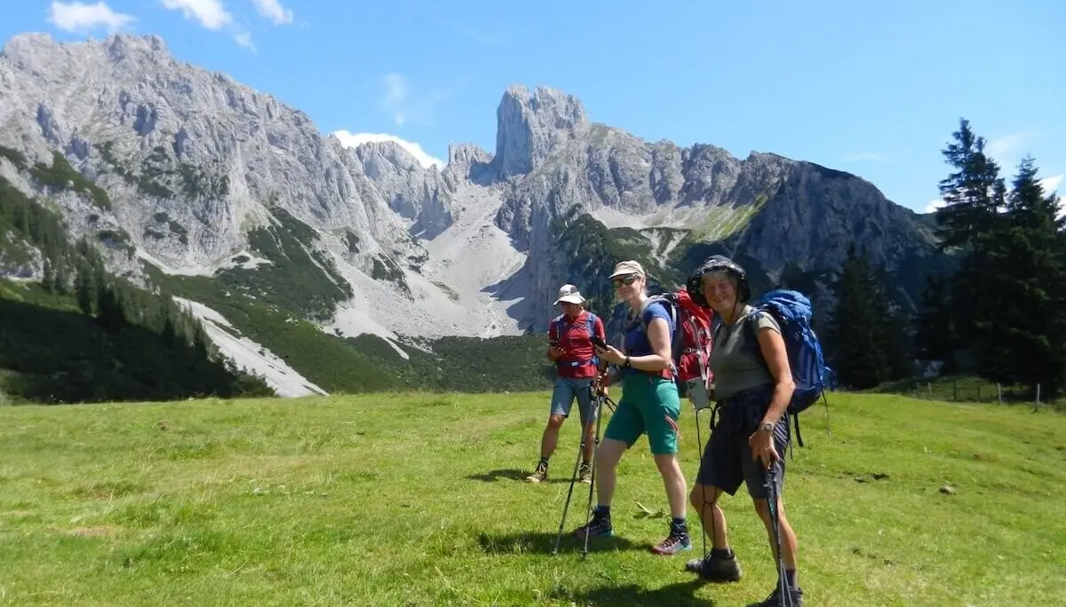 Vier Wandernde mit Stöcken und Rucksäcken stehen auf einer grünen Wiese vor steilen Felsen bei sonnigem Wetter. | © DAV Markt Schwaben | Foto: Christine Strasser