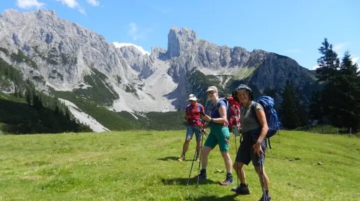 Vier Wandernde mit Stöcken und Rucksäcken stehen auf einer grünen Wiese vor steilen Felsen bei sonnigem Wetter. | © DAV Markt Schwaben | Foto: Christine Strasser