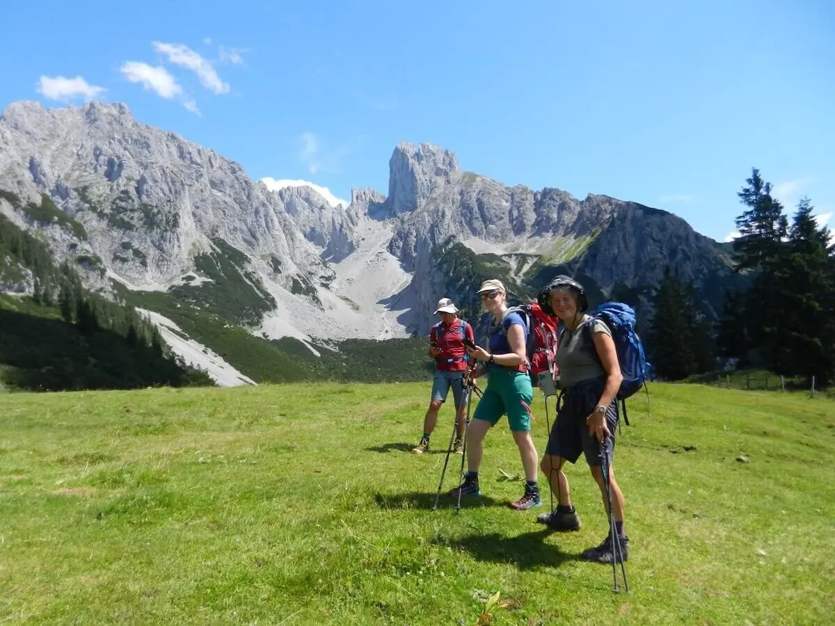 Vier Wandernde mit Stöcken und Rucksäcken stehen auf einer grünen Wiese vor steilen Felsen bei sonnigem Wetter. | © DAV Markt Schwaben | Foto: Christine Strasser