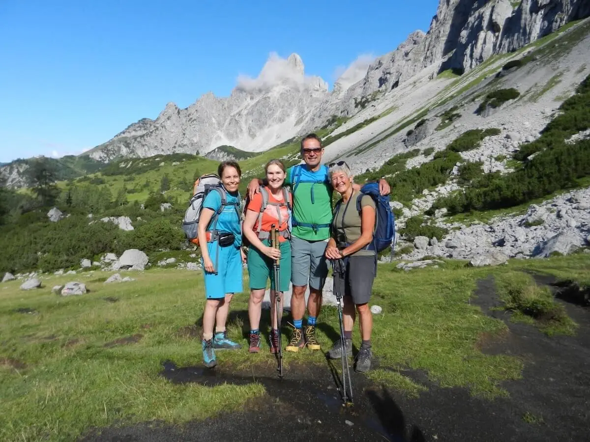 Vier Wandernde posieren in alpiner Kulisse mit Blick auf die Bischofsmütze – grüne Hügel, Fels und Wolken umrunden den Gipfel. | © DAV Markt Schwaben | Foto: Christine Strasser
