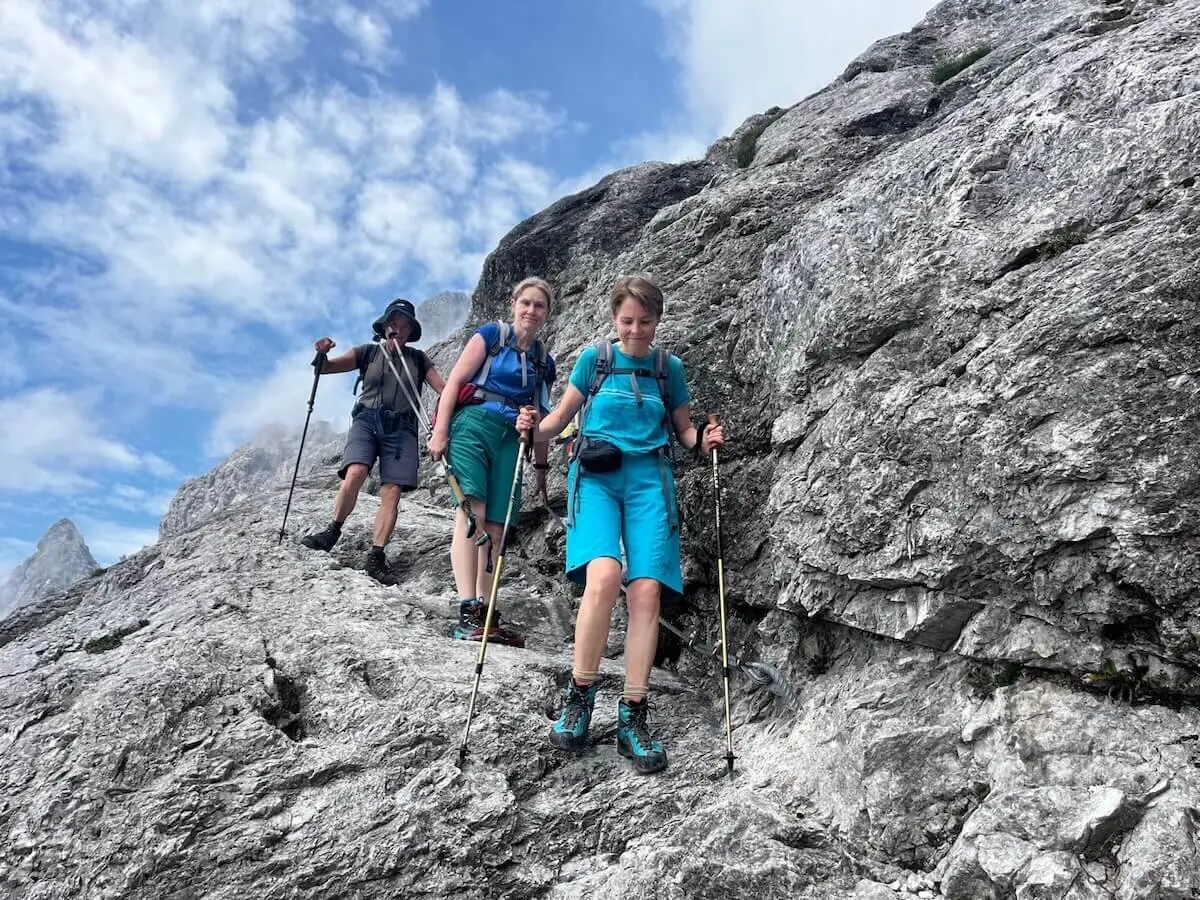 Drei Wandernde steigen auf felsigem Pfad vom Steiglpass ab – mit Trekkingausrüstung vor klarer Bergkulisse und blauem Himmel. | © DAV Markt Schwaben | Foto: Markus Sellmeier