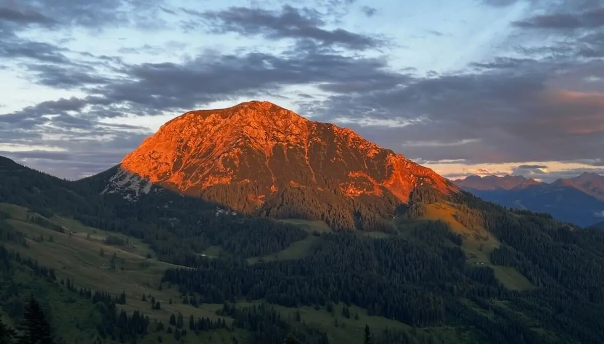 Die Hofpürglhütte liegt im Licht der Abendsonne vor bewaldeten Hängen und leuchtender Bischofsmütze unter sanft gefärbtem Himmel. | © DAV Markt Schwaben | Foto: Markus Sellmeier