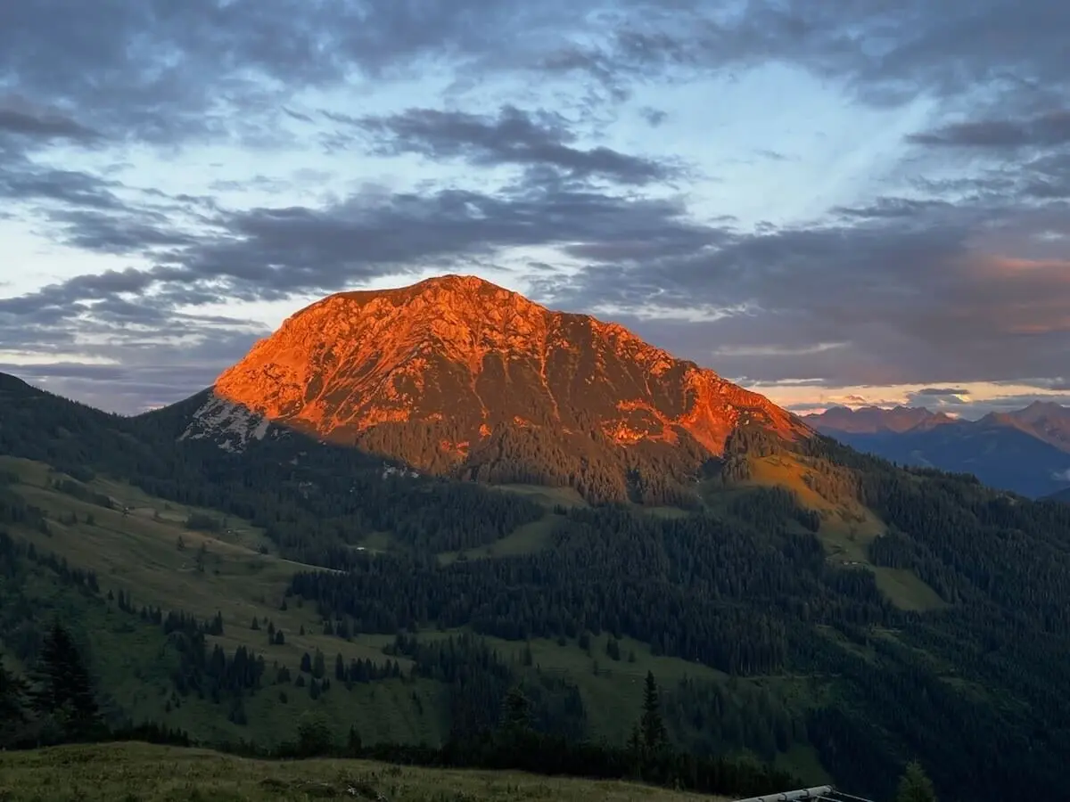 Die Hofpürglhütte liegt im Licht der Abendsonne vor bewaldeten Hängen und leuchtender Bischofsmütze unter sanft gefärbtem Himmel. | © DAV Markt Schwaben | Foto: Markus Sellmeier