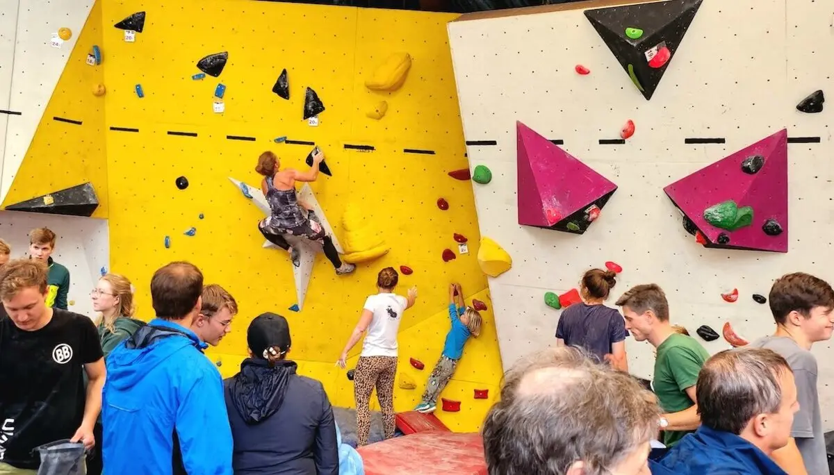 Junge und erwachsene Kletternde zeigen ihr Können an bunten Boulderwänden – Publikum beobachtet gespannt das Geschehen. | © DAV Markt Schwaben | Foto Anna Thoms