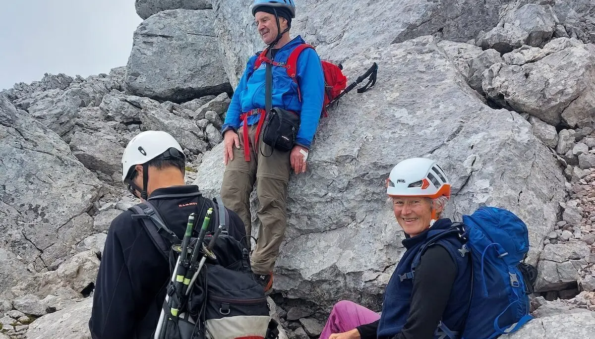 Drei Bergsteiger rasten auf felsigem Grat, einer sitzt lächelnd, hinten steiles Gelände und Waldhang. | © DAV Markt Schwaben · Foto: Lutz Gründel