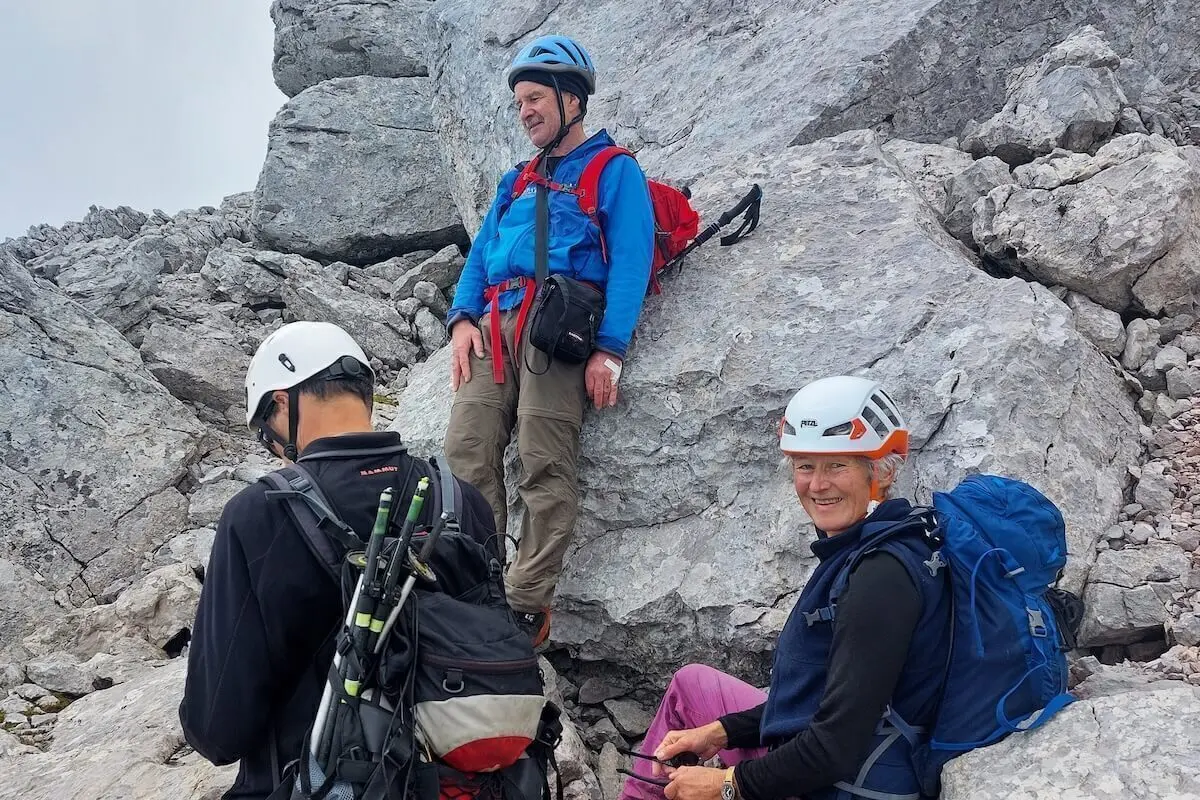 Drei Bergsteiger rasten auf felsigem Grat, einer sitzt lächelnd, hinten steiles Gelände und Waldhang. | © DAV Markt Schwaben · Foto: Lutz Gründel