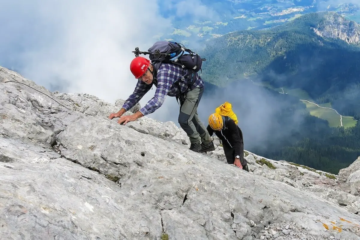Zwei Bergsteiger sichern sich am steilen Fels, hinten bewaldete Täler und Wolken über Bergflanken. | © DAV Markt Schwaben · Foto: Erwin Matzinger