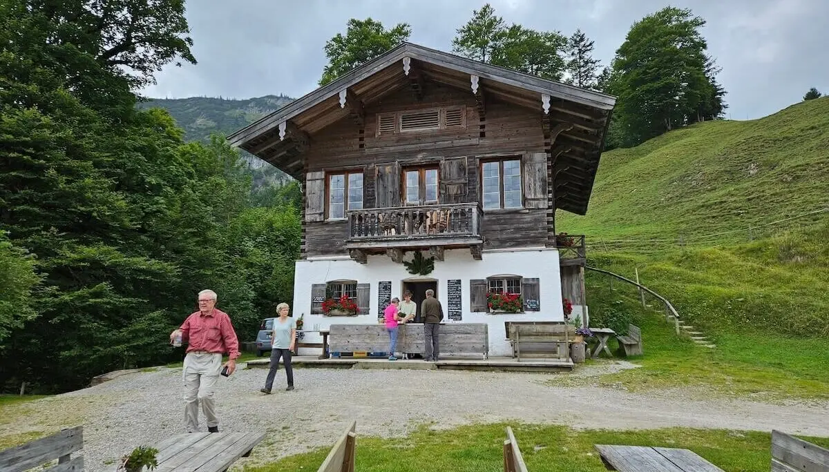 Mehrere Teilnehmende stehen vor der Königsalm mit Holzhütte, Blumenschmuck und Tischen – umgeben von alpiner Landschaft. | © DAV Markt Schwaben | Foto Hubert Inhofer