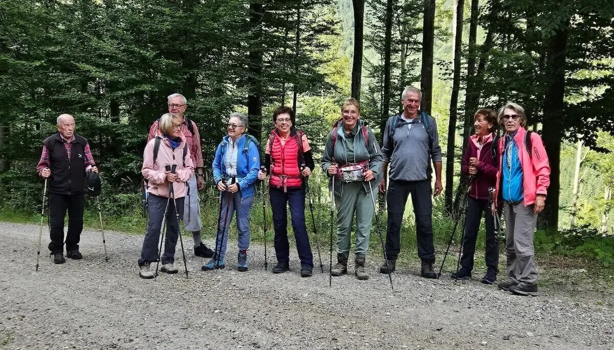Acht Wandernde stehen nebeneinander auf einem Waldweg mit dichtem Baumbestand im Hintergrund. | © DAV Markt Schwaben | Foto Hubert Inhofer