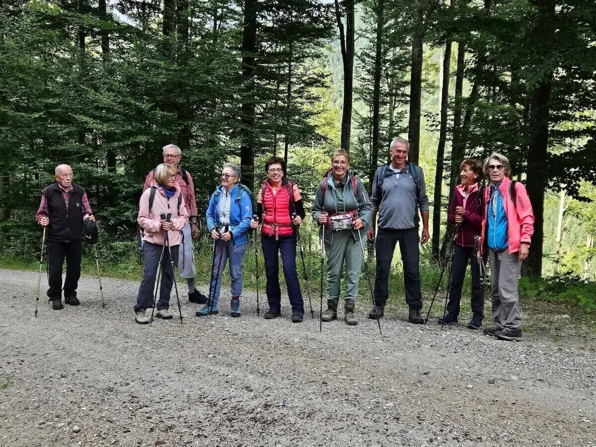 Acht Wandernde stehen nebeneinander auf einem Waldweg mit dichtem Baumbestand im Hintergrund. | © DAV Markt Schwaben | Foto Hubert Inhofer