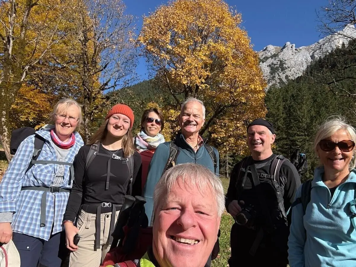 Sieben Erwachsene stehen vor herbstlich gefärbten Bäumen und Berggipfeln, lächeln in Wanderausrüstung in die Kamera. | © DAV Markt Schwaben · Foto: Markus Zimmermann