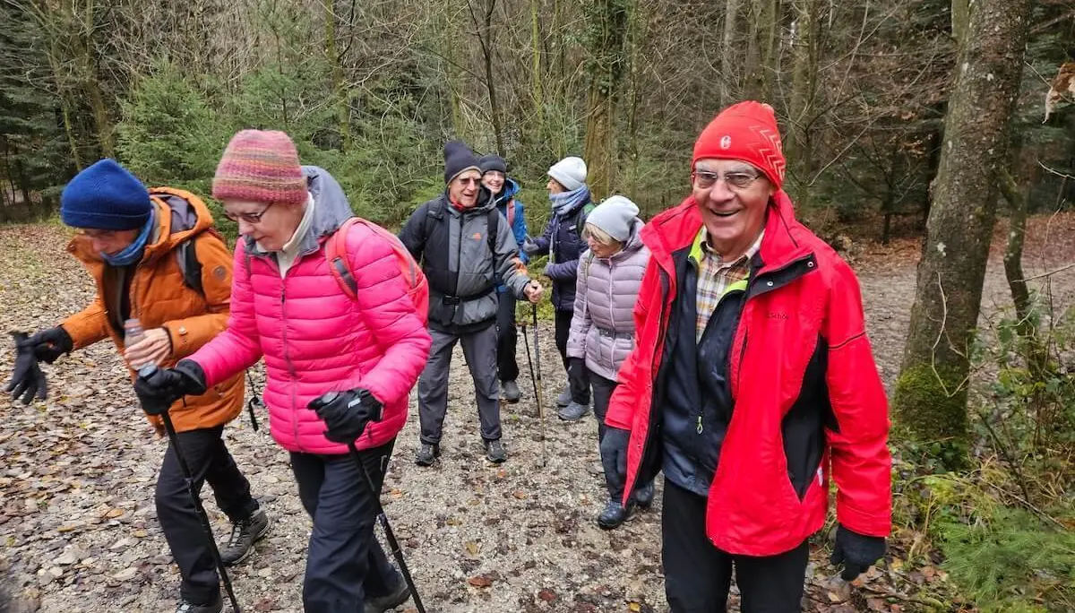 Seniorengruppe wandert bei kühlem Wetter auf einem Laubweg durch den Wald, im Vordergrund warme Kleidung und Gehstöcke. | © DAV Markt Schwaben · Foto: Hubert Inhofer