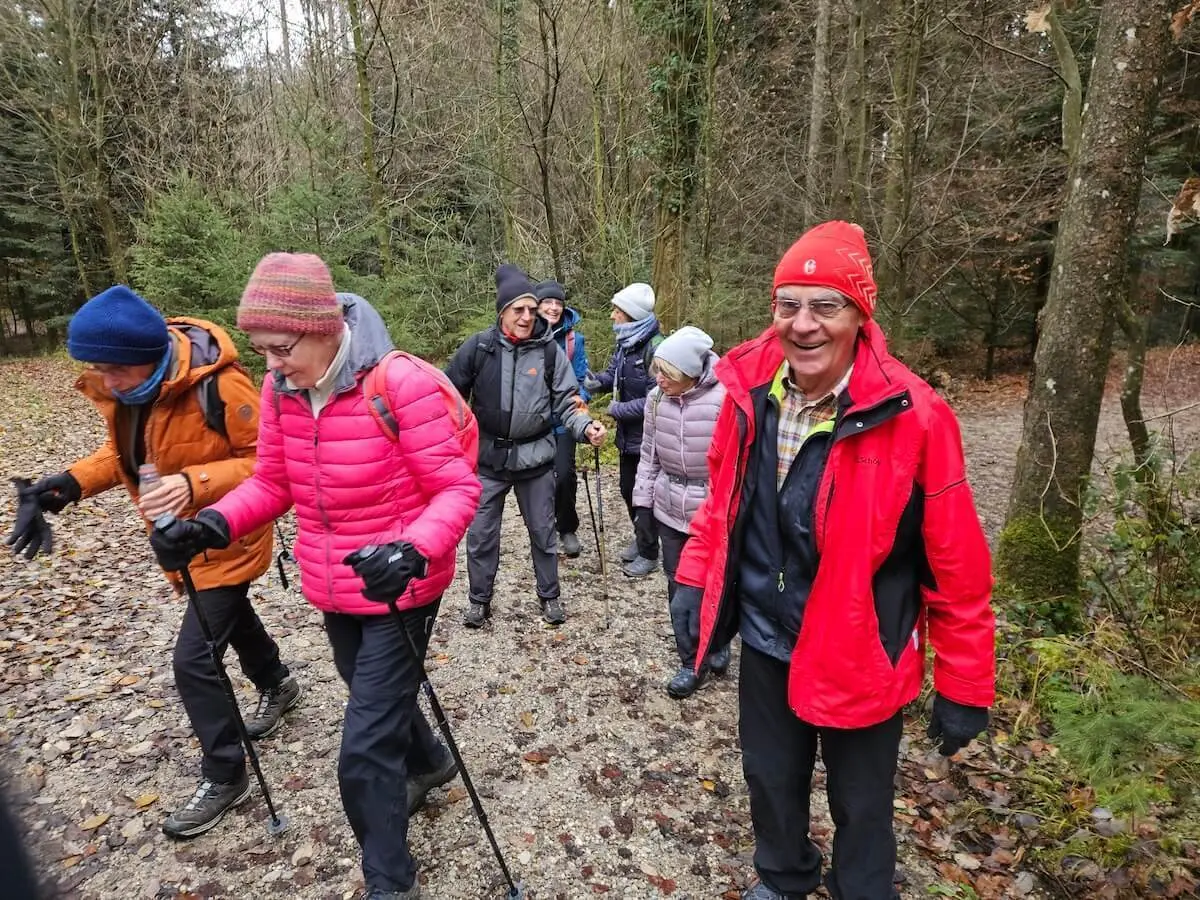 Seniorengruppe wandert bei kühlem Wetter auf einem Laubweg durch den Wald, im Vordergrund warme Kleidung und Gehstöcke. | © DAV Markt Schwaben · Foto: Hubert Inhofer