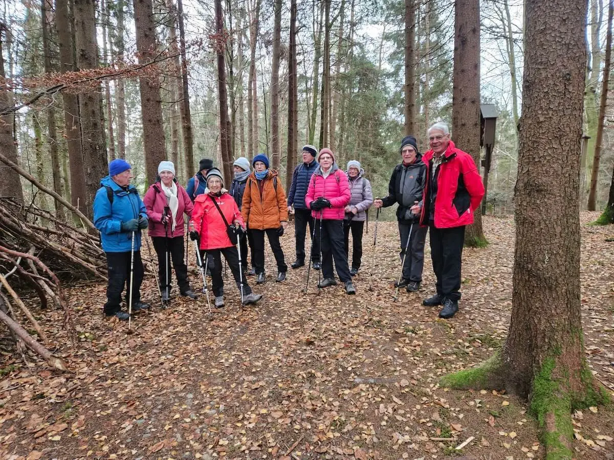 Zwölf Senioren stehen in Winterkleidung auf einem Laubweg im Wald, im Hintergrund hohe Bäume und Aststruktur. | © DAV Markt Schwaben · Foto: Hubert Inhofer
