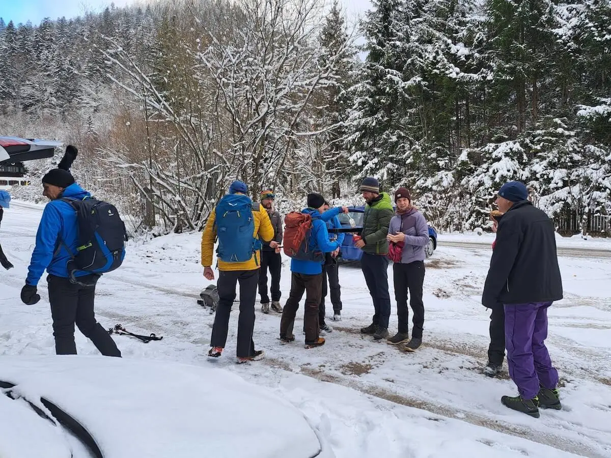 Winterwandergruppe mit Rucksäcken und Stöcken steht auf verschneitem Waldboden, Bäume und Fahrzeug im Hintergrund. | © DAV Markt Schwaben · Foto Tanja Döhler