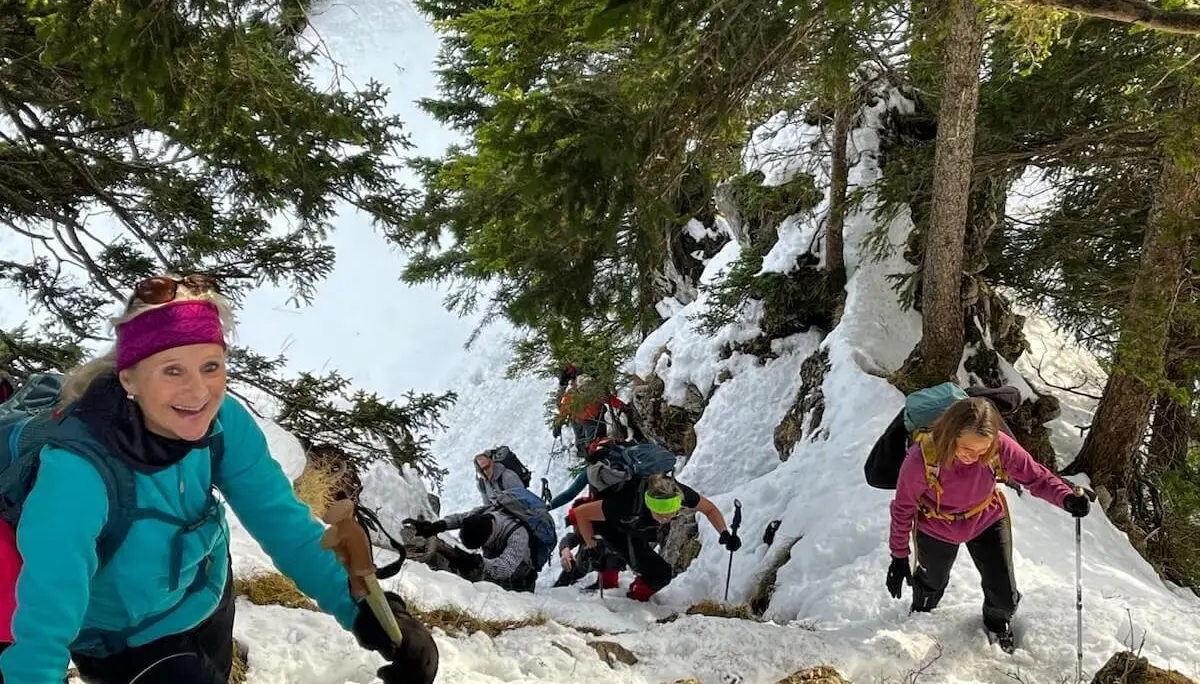 Eine Wanderin mit Winterausrüstung steigt einen steilen, verschneiten Bergpfad hinauf, umgeben von Nadelbäumen. Die Szene zeigt die anspruchsvolle Passage in alpinem Gelände. | © DAV Markt Schwaben · Foto Markus Sellmeier