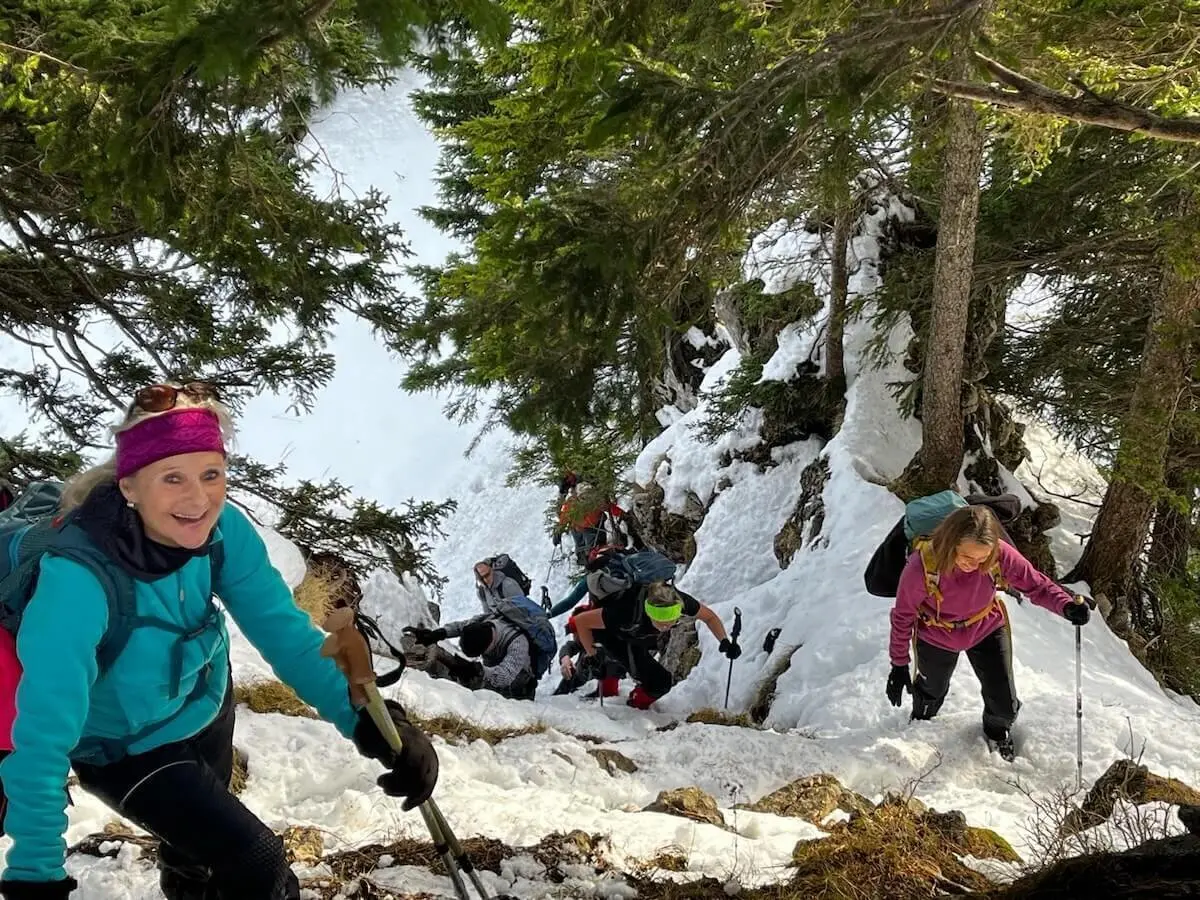 Eine Wanderin mit Winterausrüstung steigt einen steilen, verschneiten Bergpfad hinauf, umgeben von Nadelbäumen. Die Szene zeigt die anspruchsvolle Passage in alpinem Gelände. | © DAV Markt Schwaben · Foto Markus Sellmeier