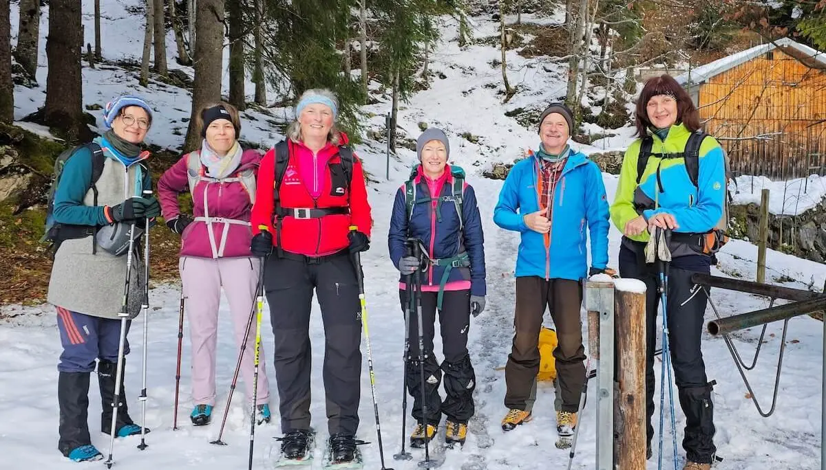 Sechs Wandernde stehen mit Winterausrüstung vor einer Holzhütte; verschneiter Waldboden und Tannen im Hintergrund. | © DAV Markt Schwaben | Foto: Lutz Gründel