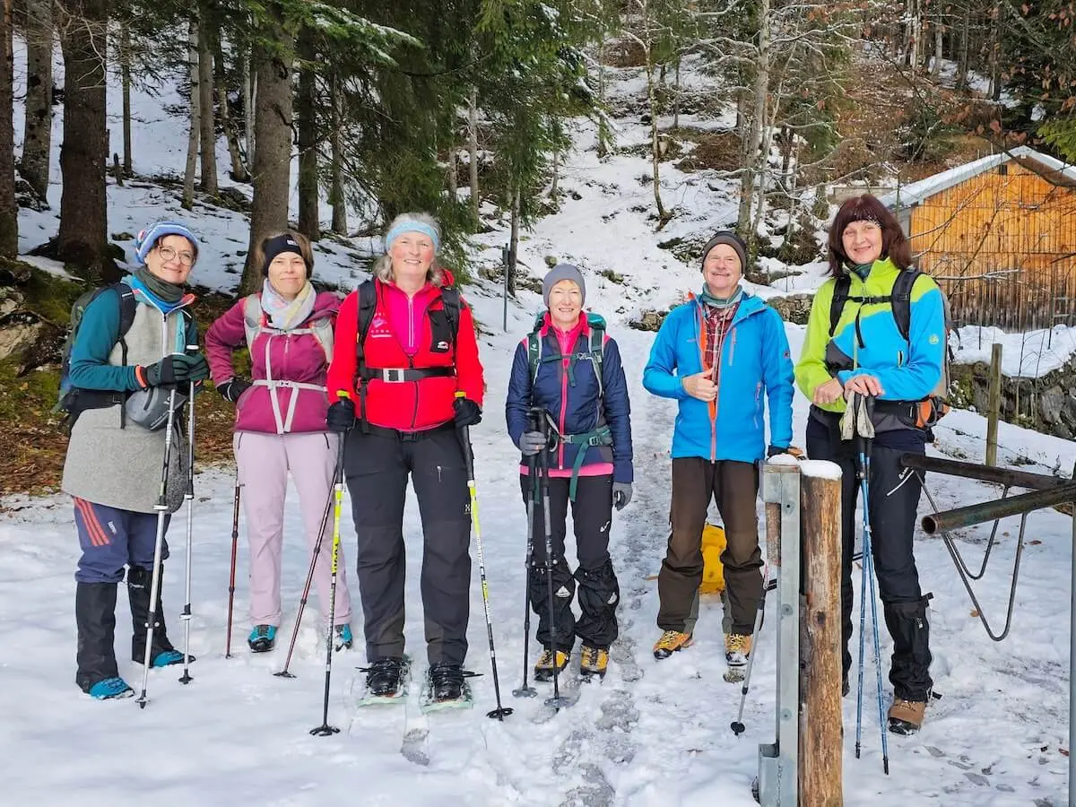 Sechs Wandernde stehen mit Winterausrüstung vor einer Holzhütte; verschneiter Waldboden und Tannen im Hintergrund. | © DAV Markt Schwaben | Foto: Lutz Gründel