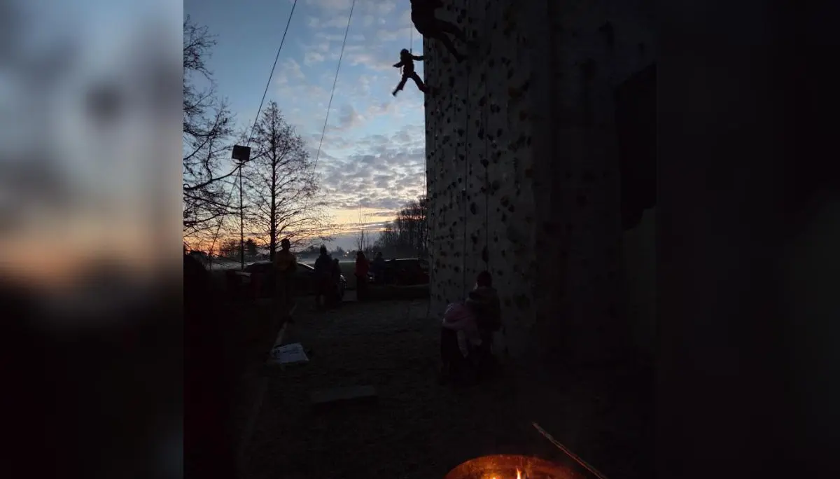 Kinder und Erwachsene beim Klettern an der beleuchteten Wand; im Vordergrund Feuerschale, dahinter Abendhimmel und Bäume. | © DAV Markt Schwaben · Familiengruppe