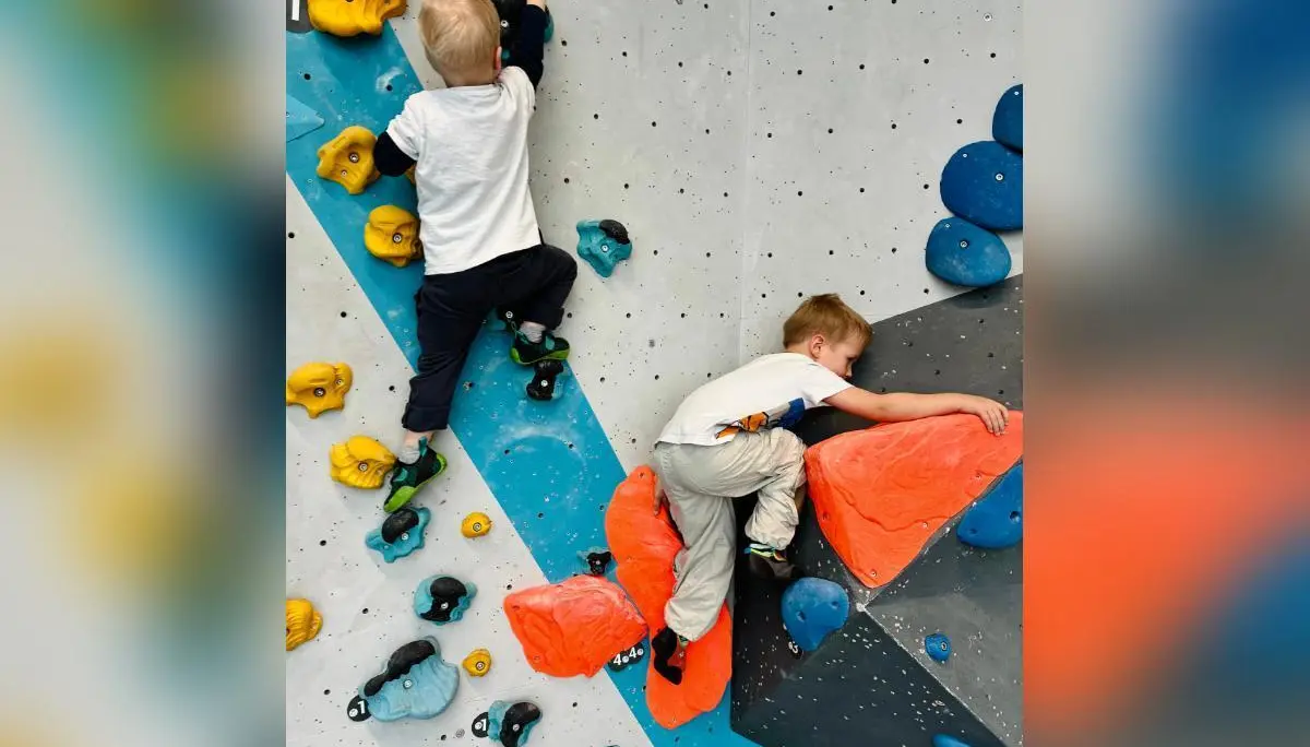 Zwei Kinder klettern konzentriert an bunten Bouldergriffen; geometrisch gestaltete Wand im Hintergrund zeigt Routenvielfalt. | © DAV Markt Schwaben/Lara Wolff