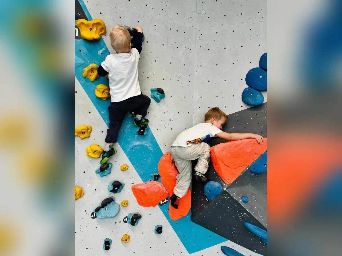 Zwei Kinder klettern konzentriert an bunten Bouldergriffen; geometrisch gestaltete Wand im Hintergrund zeigt Routenvielfalt. | © DAV Markt Schwaben/Lara Wolff