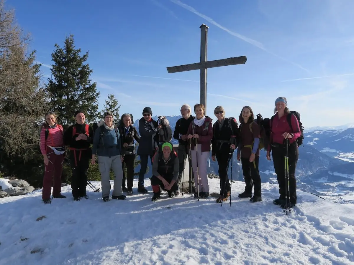 Elf Erwachsene stehen auf dem verschneiten Gipfel neben einem großen Holzkreuz und blicken vor klarer Bergkulisse in die winterlichen Alpen. | © DAV Markt Schwaben/Erwin Matzinger