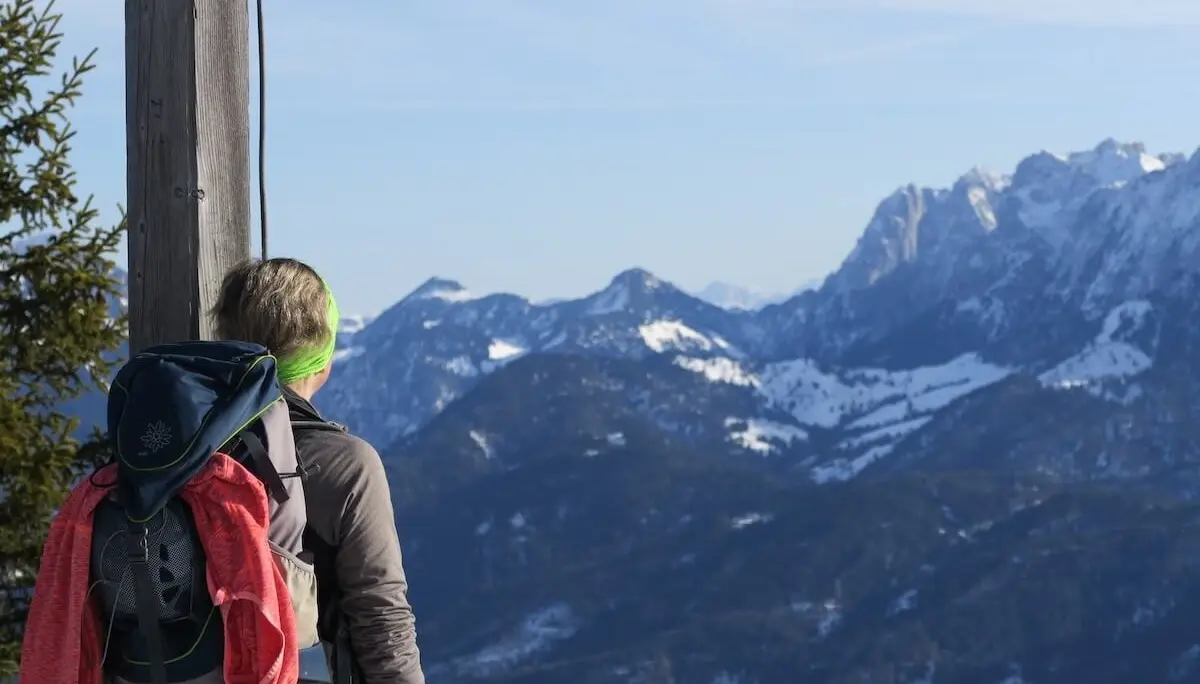 Eine Person steht mit Rucksack am verschneiten Bergpfad neben einem Holzpfosten und schaut über die weiten, klaren Alpen mit schneebedeckten Gipfeln. | © DAV Markt Schwaben/Erwin Matzinger