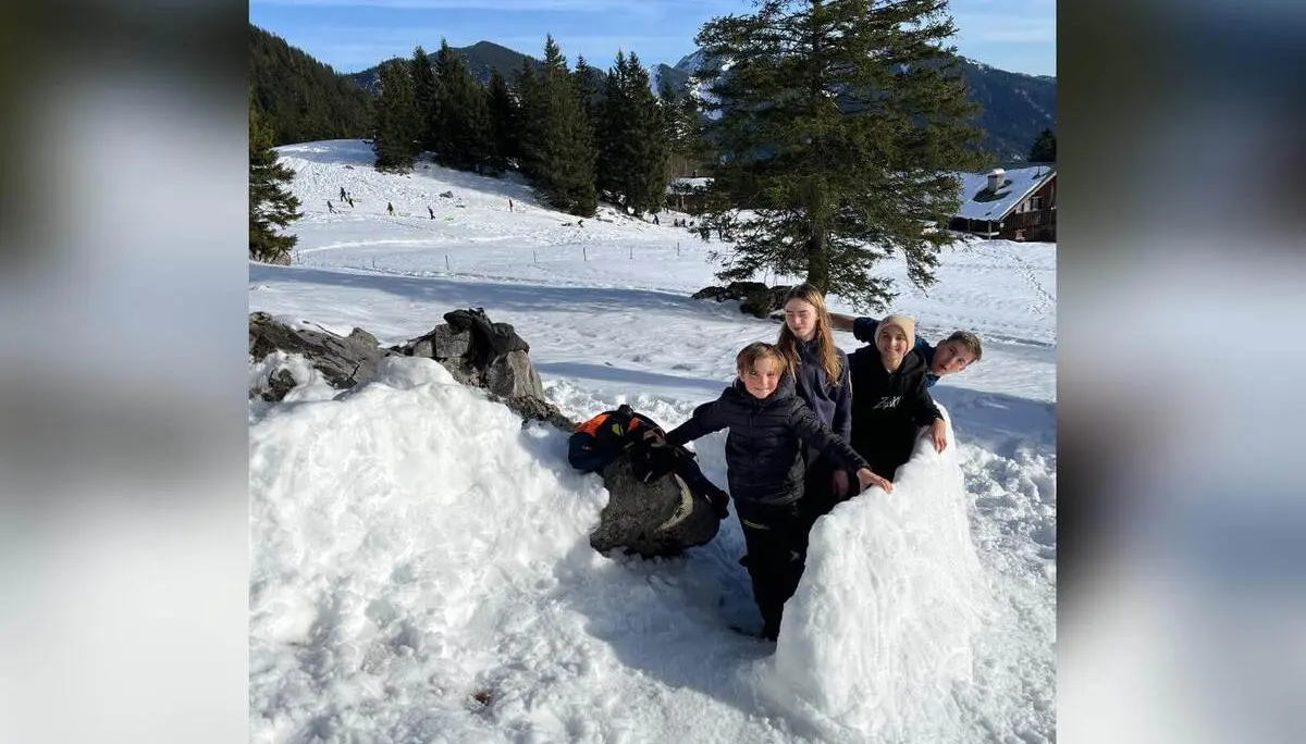 Fünf Jugendliche der Jugendgruppen Bergdohlen stehen im Schnee neben großen Schneehügeln, im Hintergrund verschneite Wiesen, Bäume und Berge bei Sonnenschein. | © DAV Markt Schwaben / Wiebke Rauschenbach